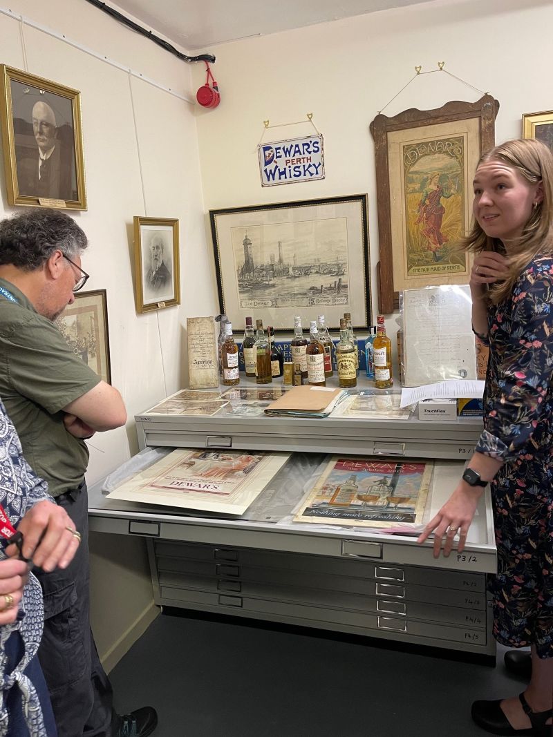 Archivist, Samantha Case (pictured on the right), shows the group a selection of original advertising posters for John Dewar & Sons Ltd